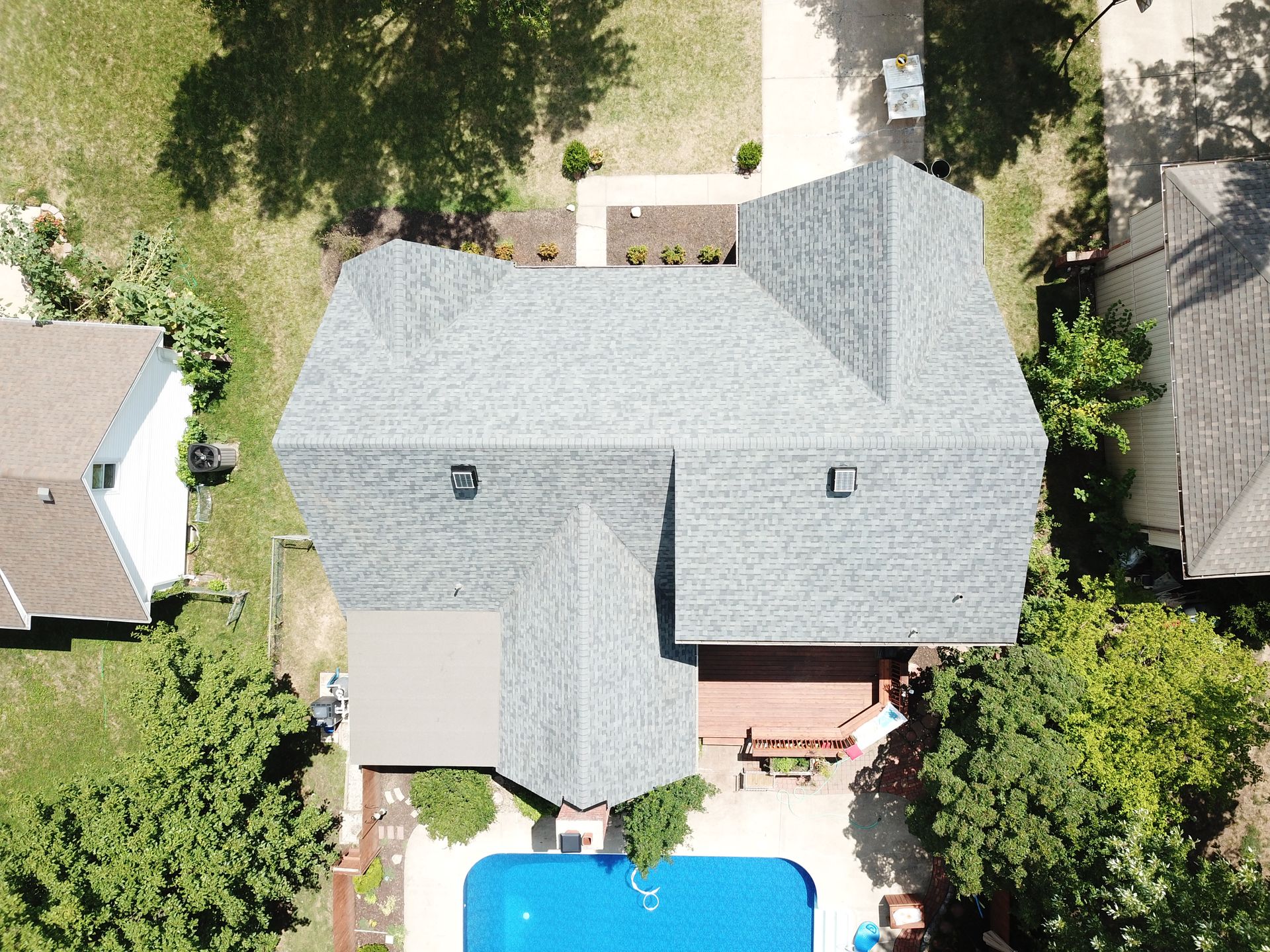 Overhead view of a house with a gray roof, a pool, and green yard on a sunny day.
