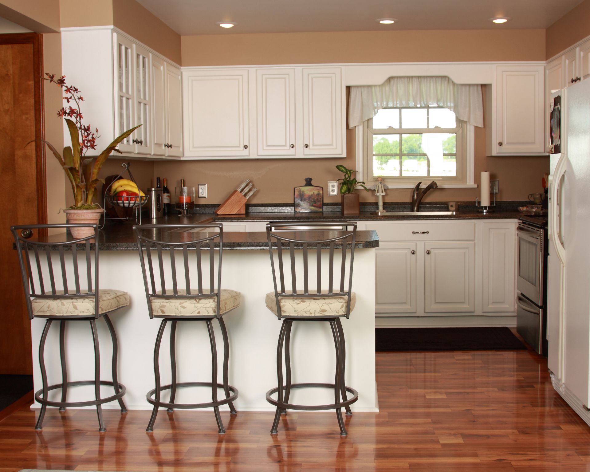Kitchen with white cabinets, dark countertops, and three bar stools.