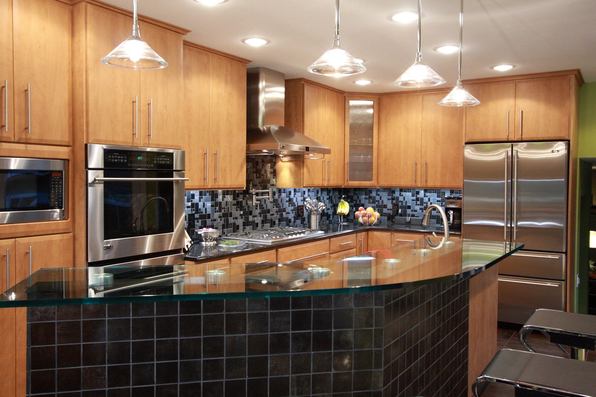Modern kitchen with light wood cabinets, stainless steel appliances, and black tile island.