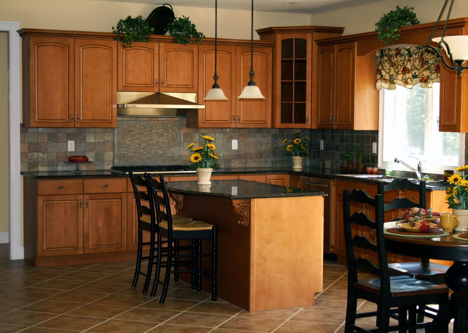 Kitchen with wood cabinets, island, black countertops, and a dining table.