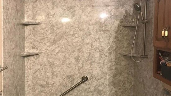 Shower stall with grab bar, two shelves, and a handheld showerhead. Gray marbled walls, brown cabinet.