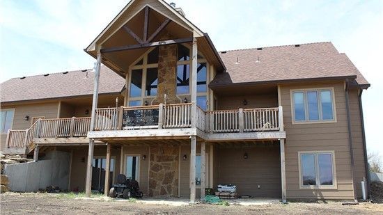 Brown two-story house with a large window facade, balconies, and a stone facade on the lower level.