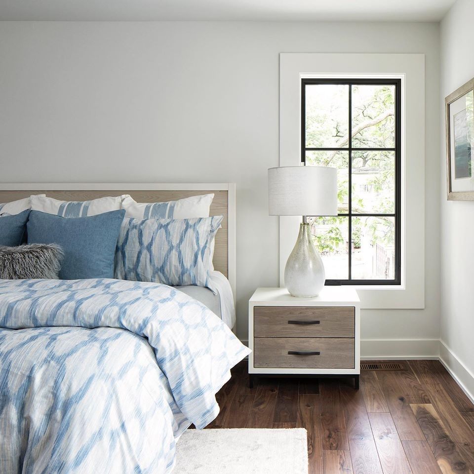 Bedroom with blue bedding, white nightstand, dark wood floors, and a window.