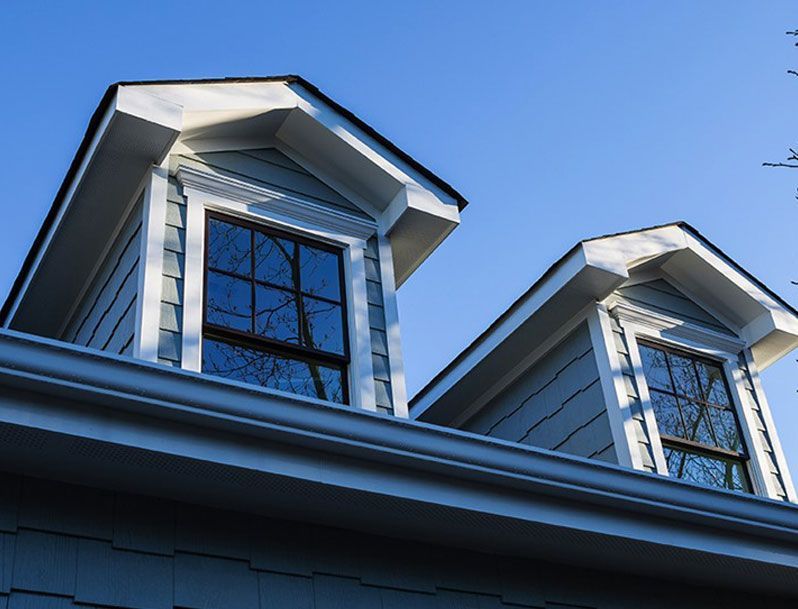 Two blue-grey dormer windows with white trim against a clear blue sky.