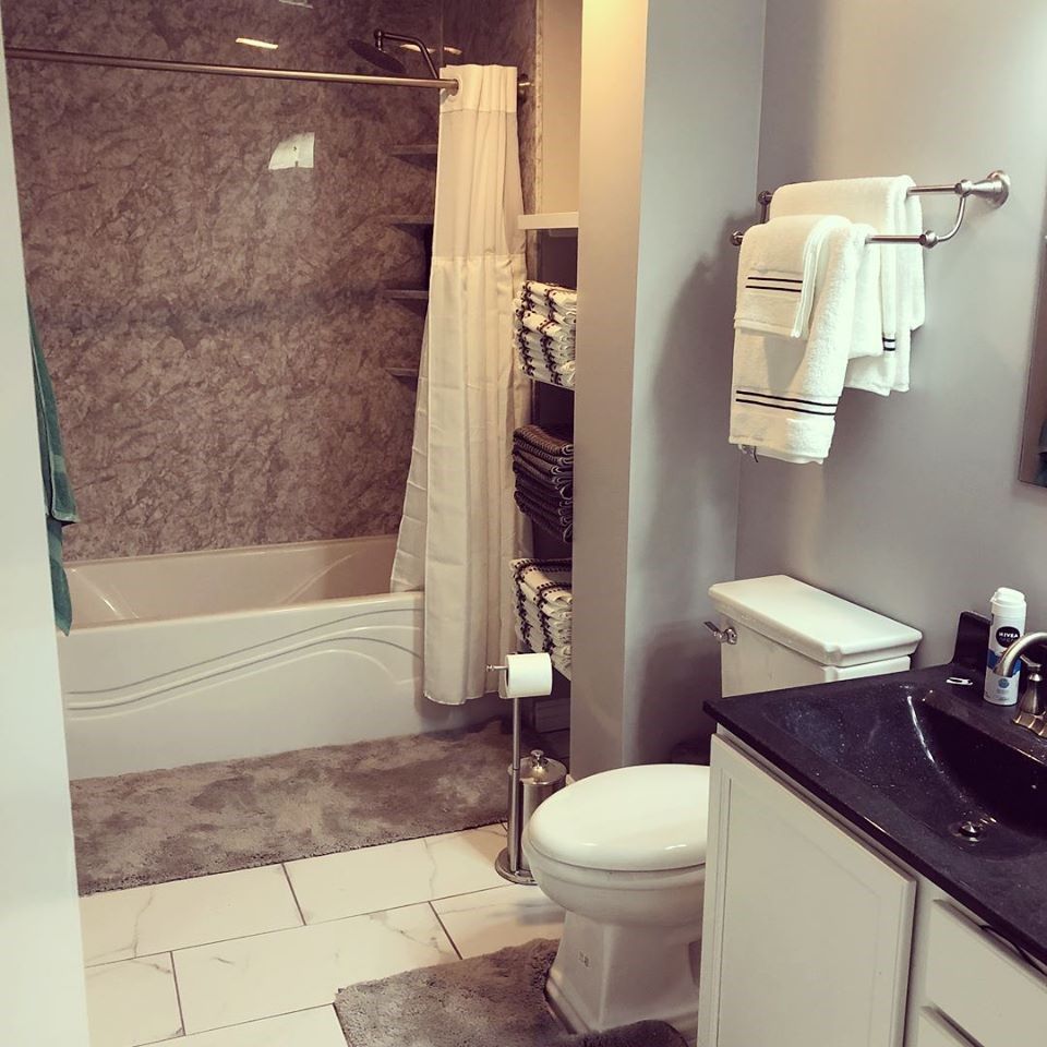 Bathroom with tub, toilet, and sink. Gray walls, white fixtures, and towels.