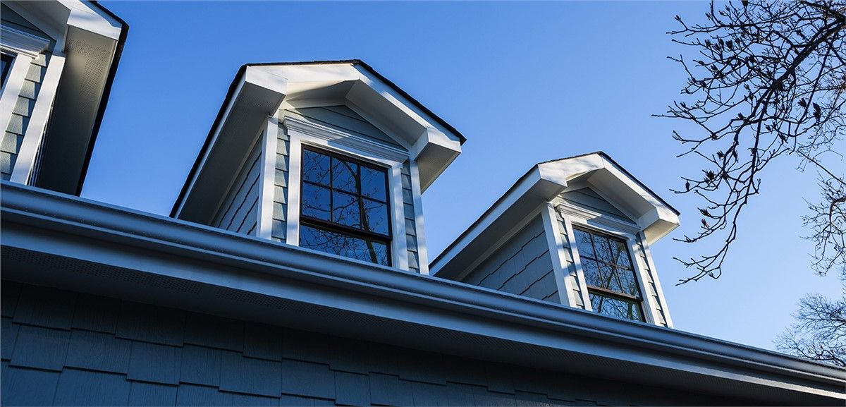 Blue-sided house with dormers against a clear, blue sky.  Tree branches on the right.