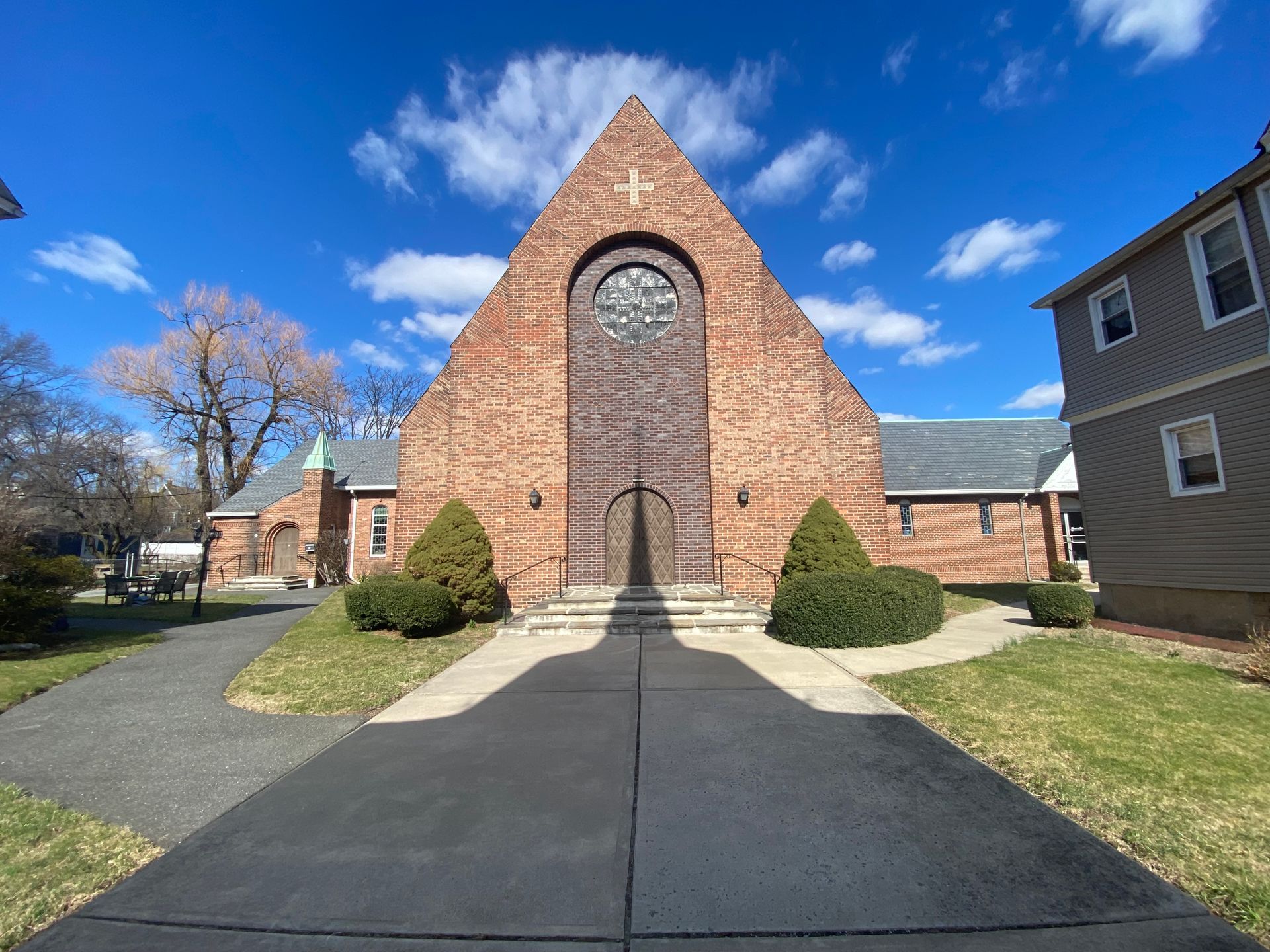 A brick church with a stained glass window is surrounded by houses on a sunny day.