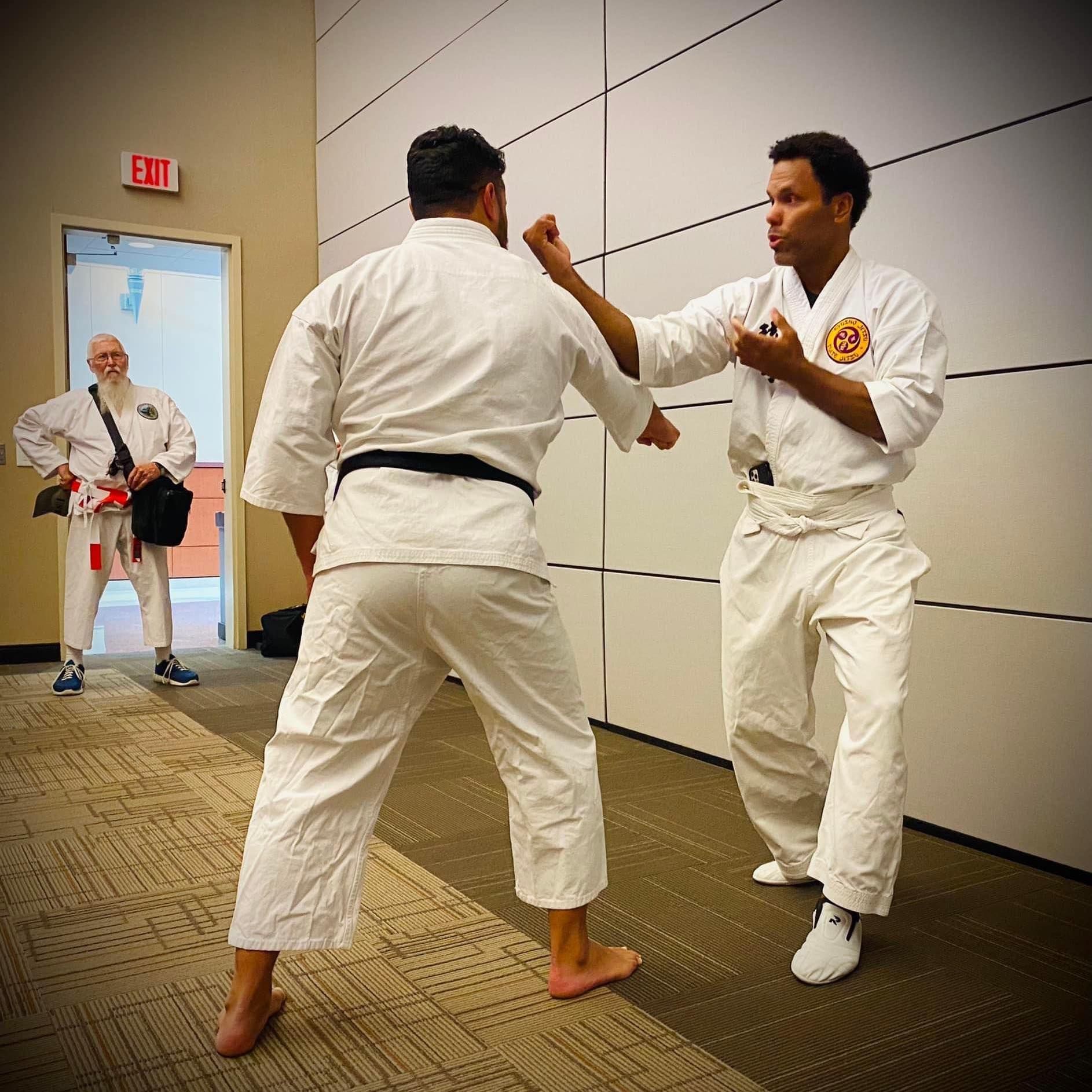 Two men are practicing karate in a room with an exit sign in the background