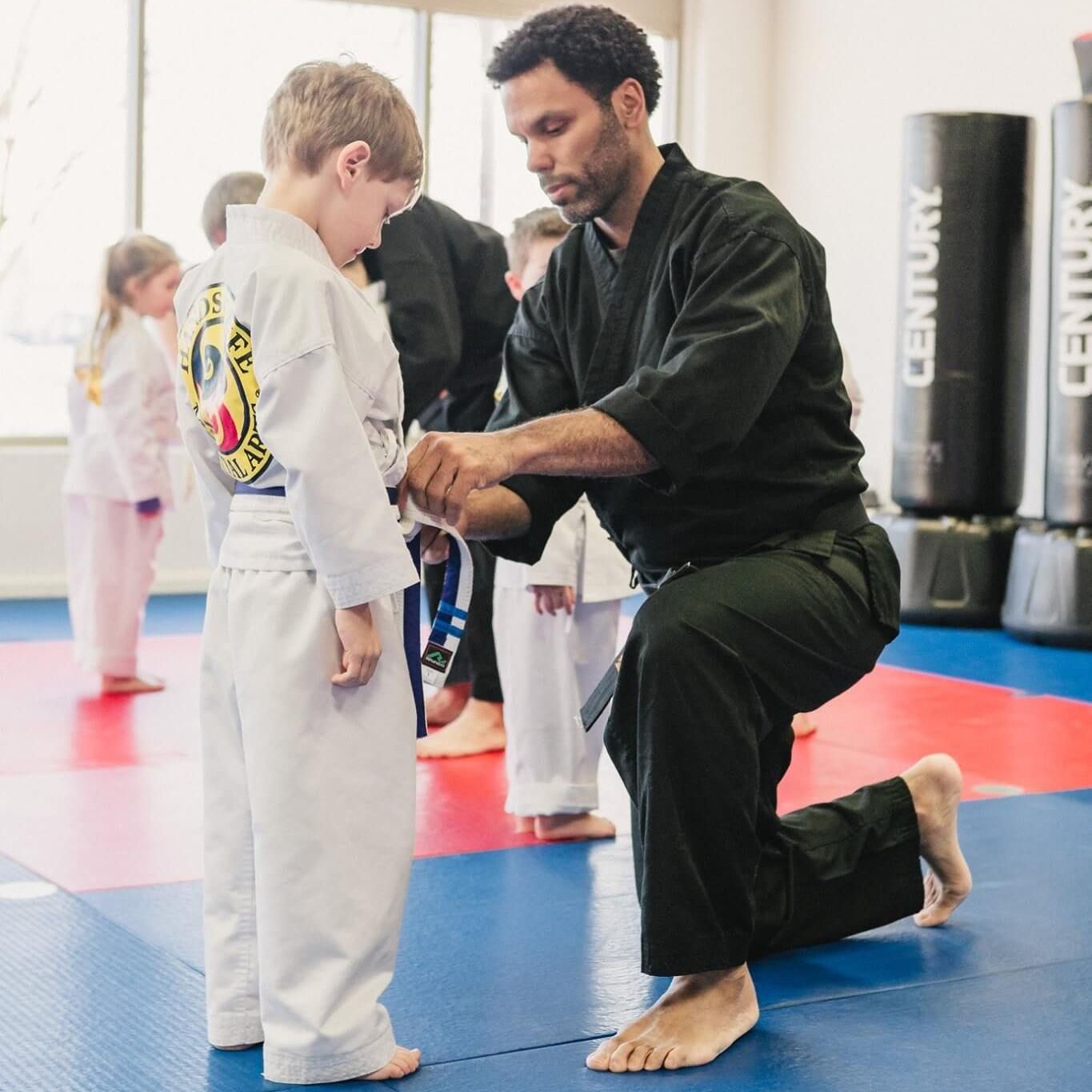 A man is helping a young boy with his martial arts belt