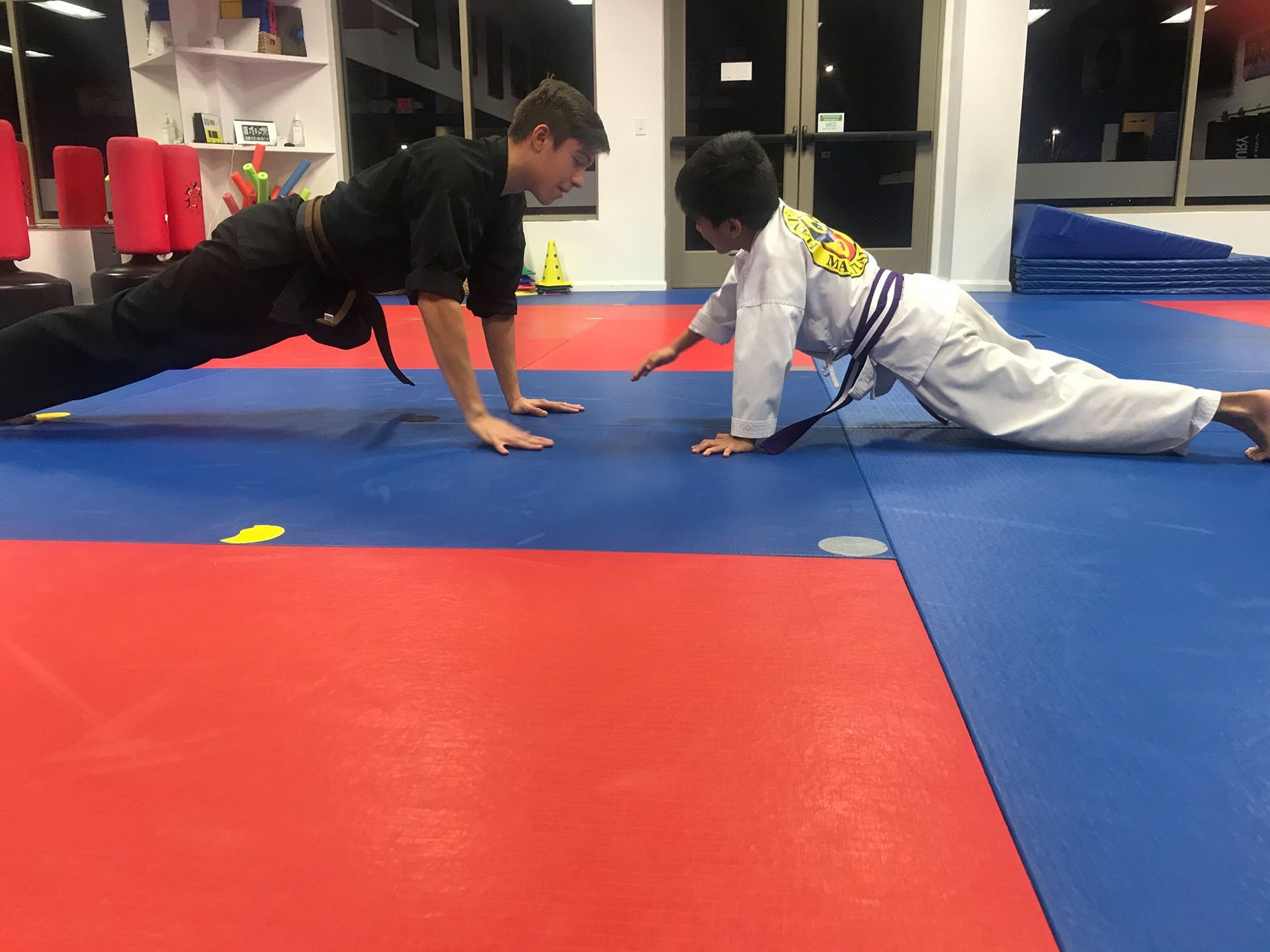 A man and a child are doing push ups on a mat in a gym.