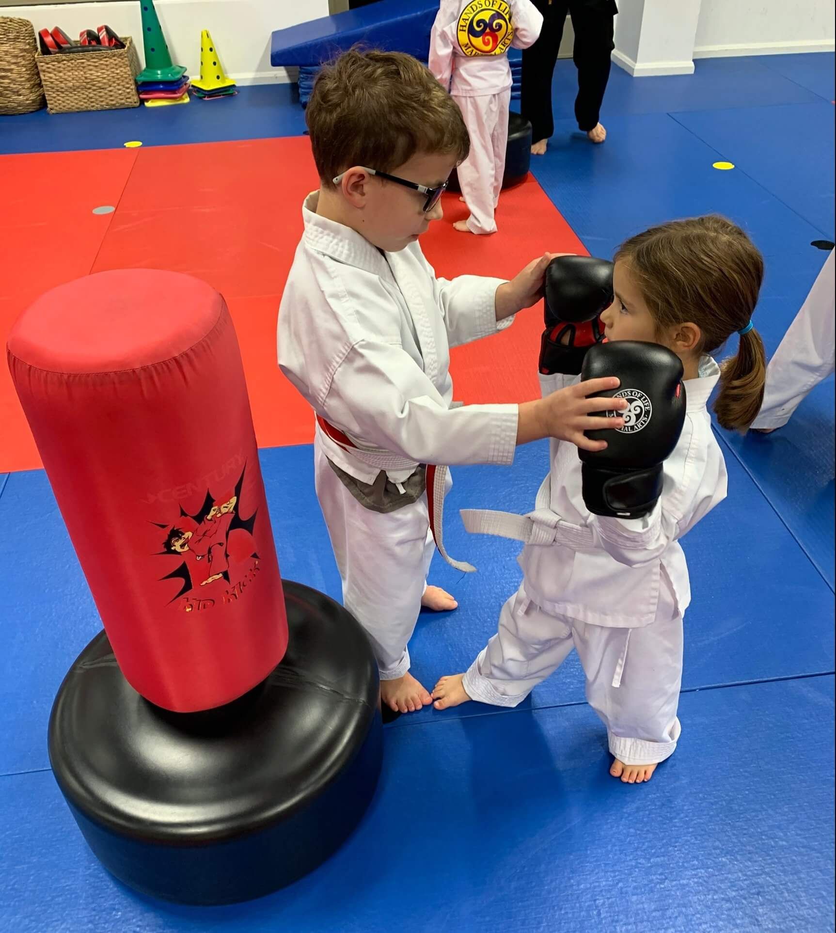 A boy and a girl are playing with boxing gloves in a gym