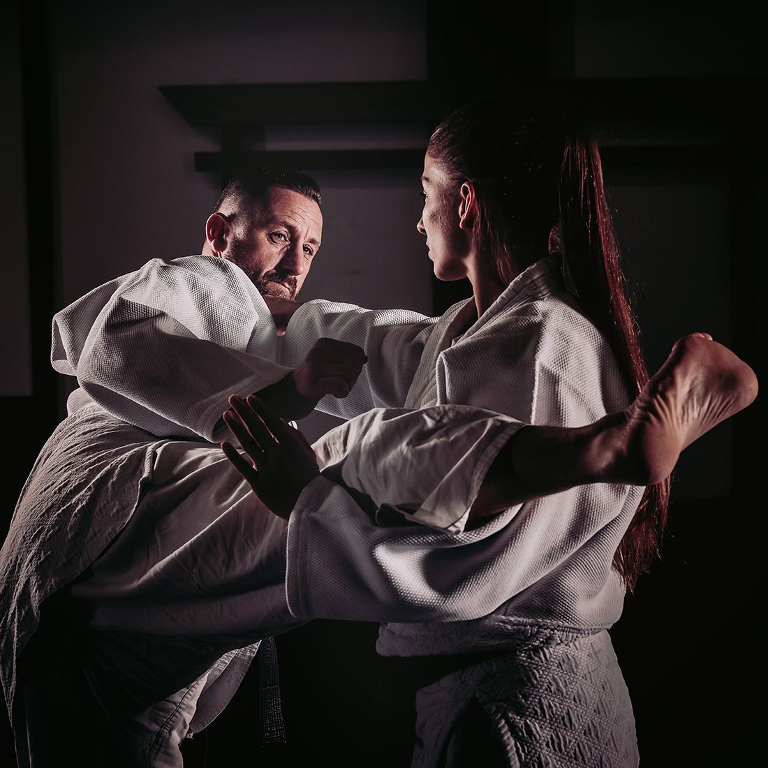 A man and a woman are practicing martial arts in a dark room.