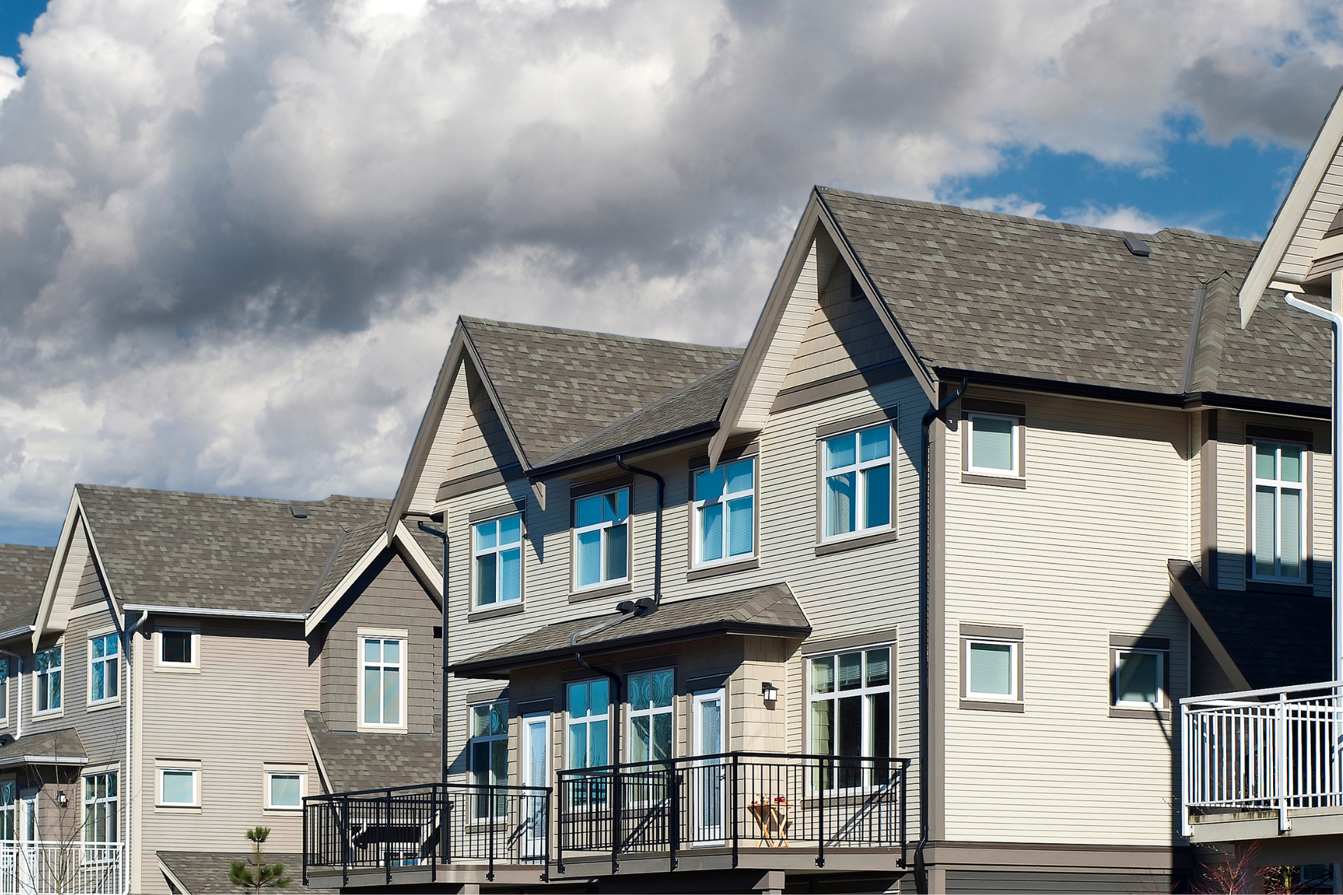 Row of townhouses with gray roofs and siding, blue sky, and clouds.