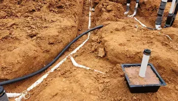 Trenches dug in dirt with black and white pipes, likely for utilities.