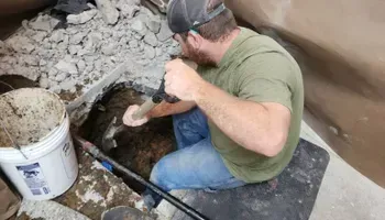Man excavating in a dark hole, using a hammer and sitting on a mat.