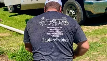 Man wearing a Stewart's Septic Services t-shirt outdoors, facing away from the camera.