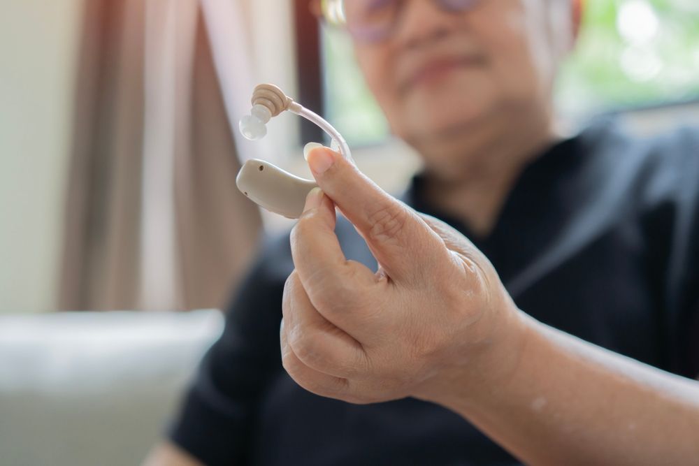 Person holding a beige hearing aid, indoors.