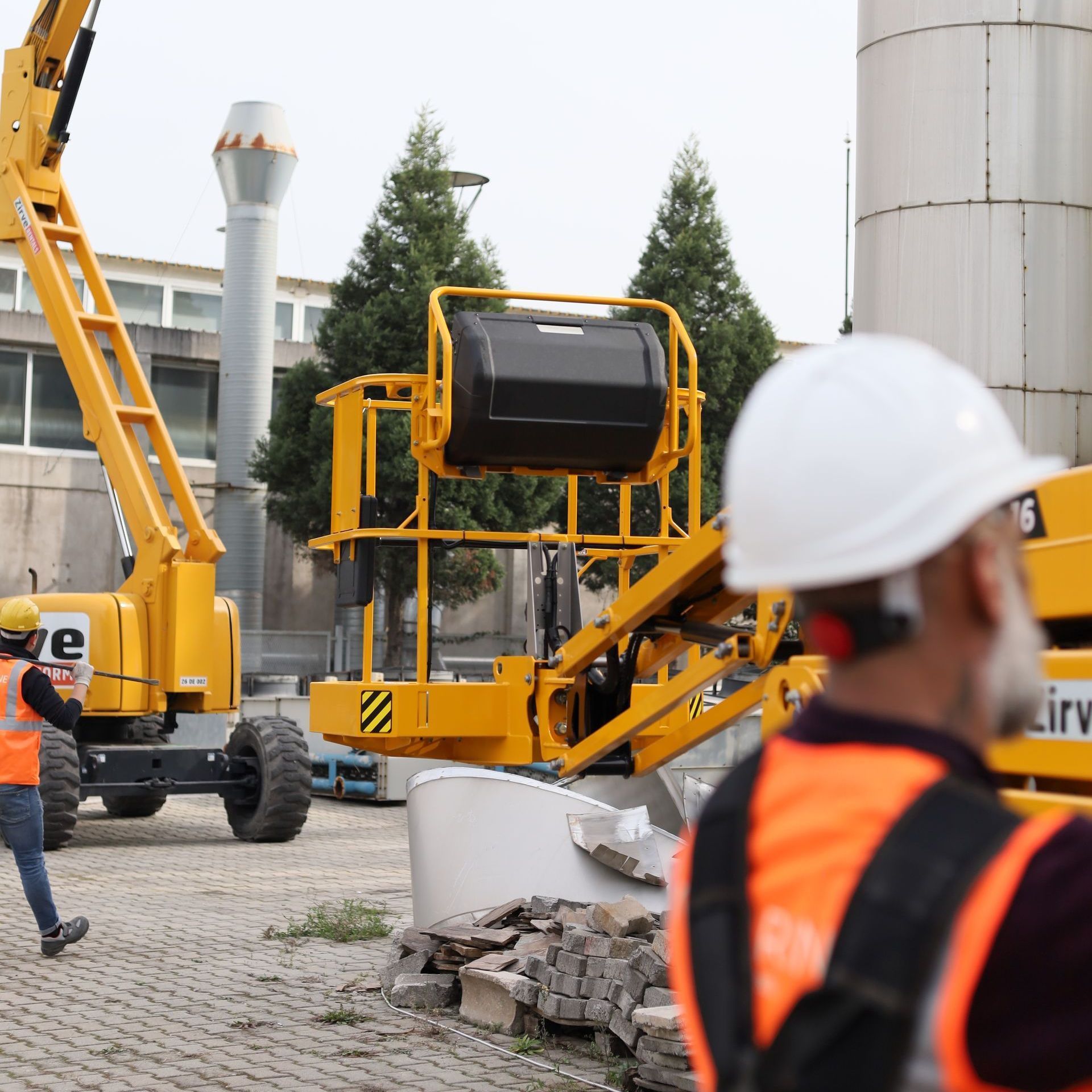 A man wearing a hard hat stands in front of a yellow crane that says irw on it