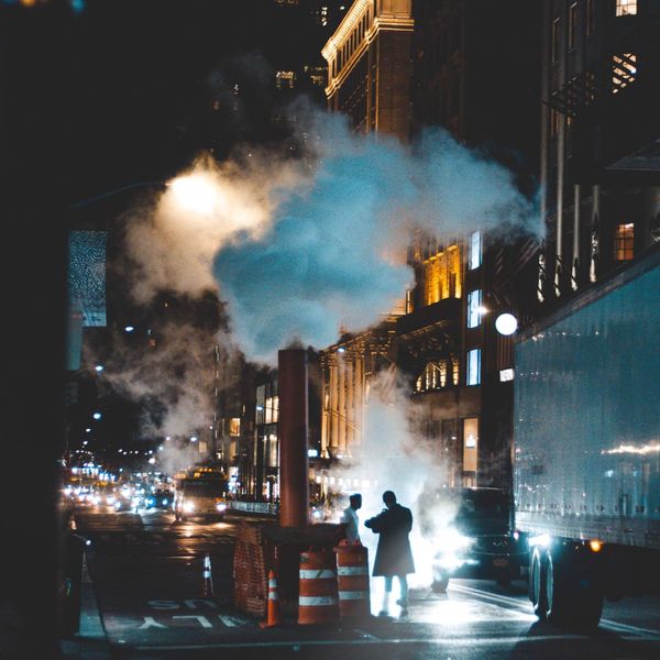 A city street at night with smoke coming out of a pipe
