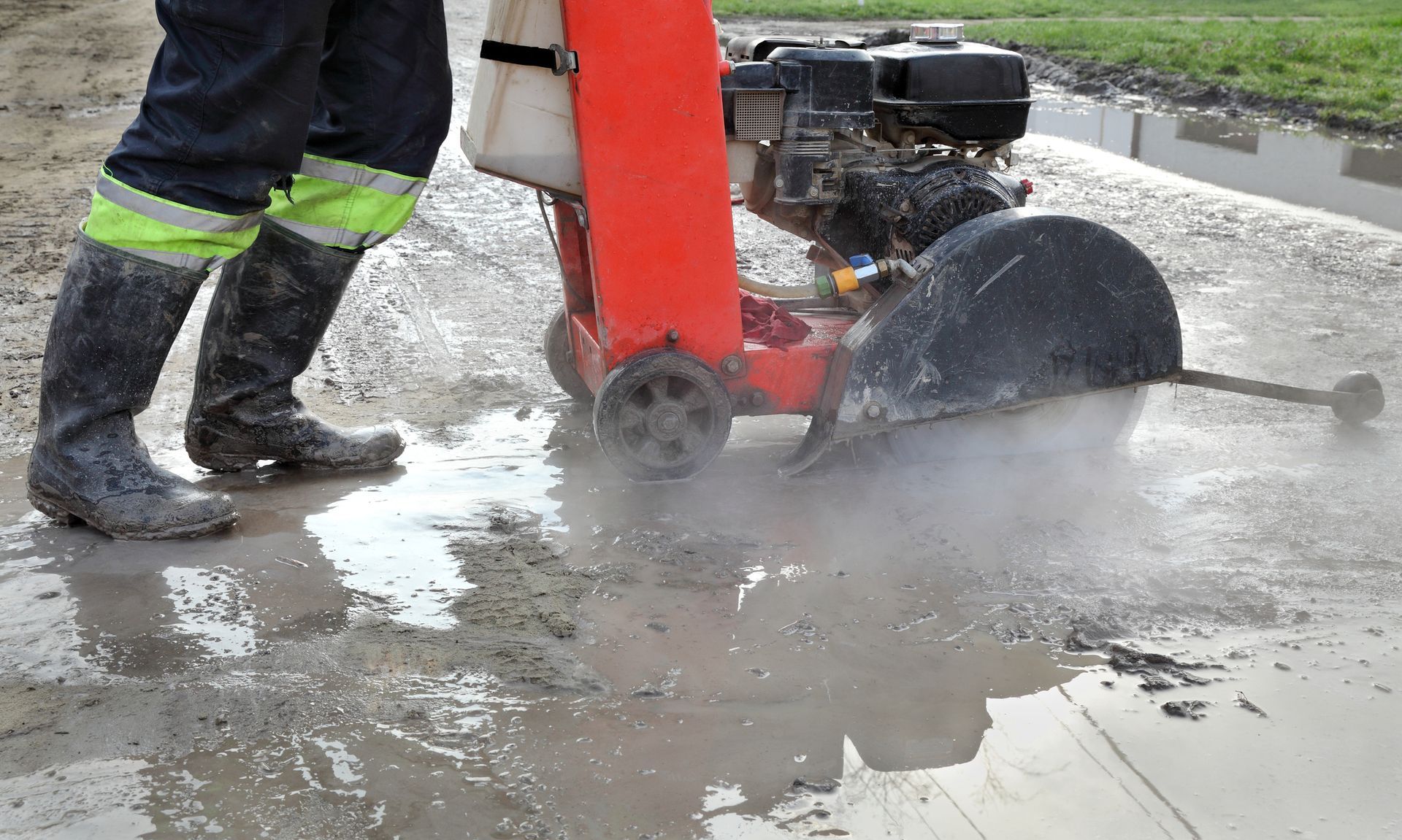 A person is using a concrete saw to cut a hole in the ground.