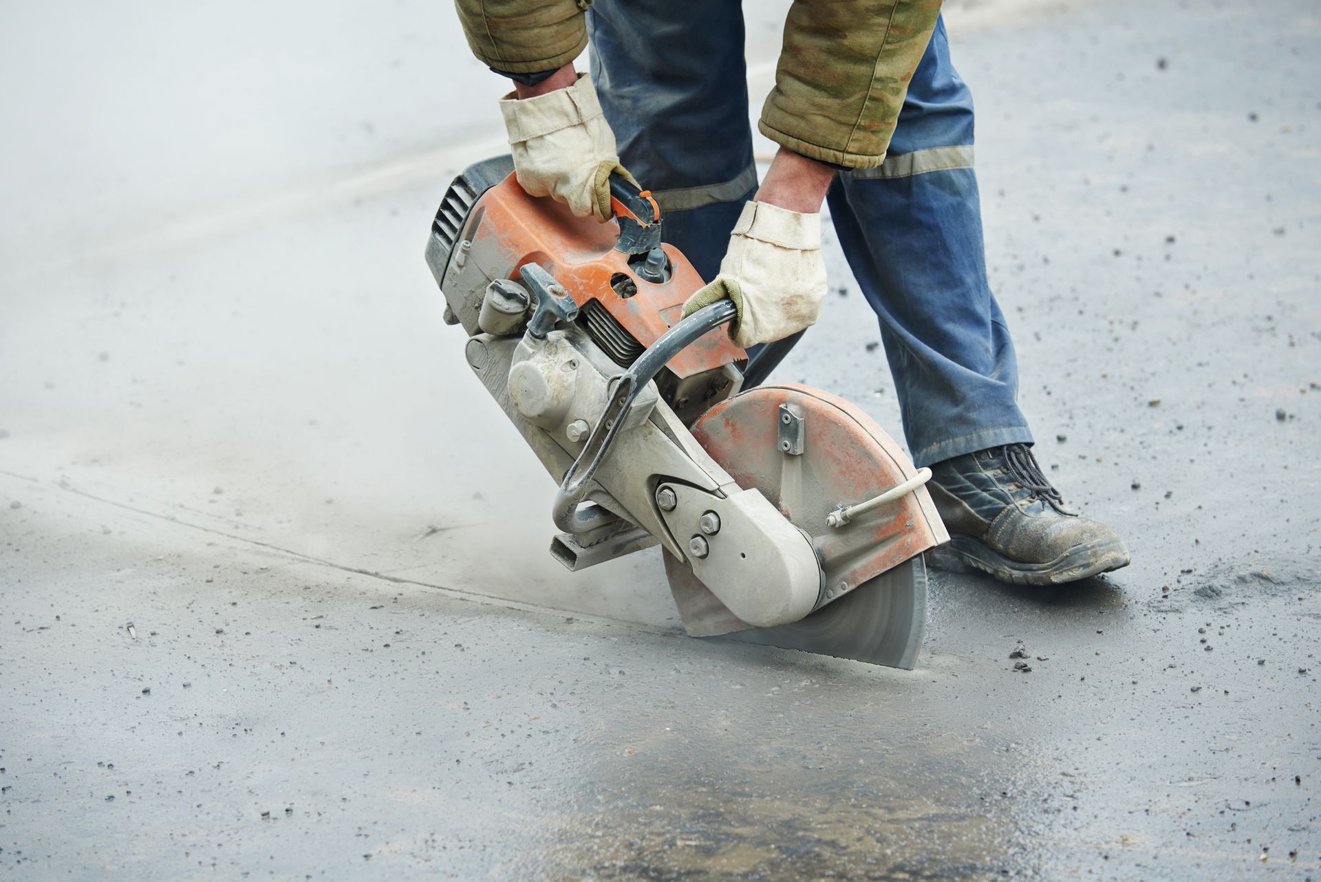 A man is using a circular saw to cut a hole in the road.