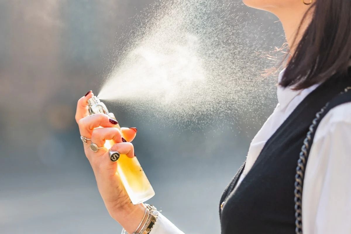 Una donna si sta spruzzando del profumo sul viso.