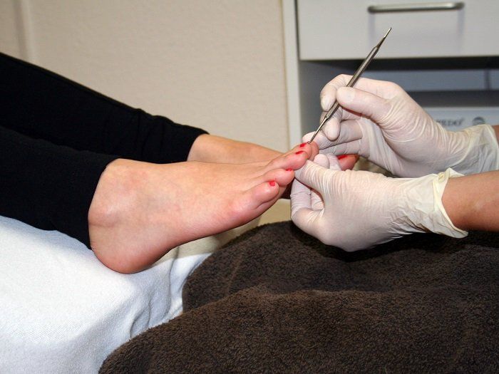 Eine Frau lässt sich von einer Person mit Handschuhen die Nägel machen