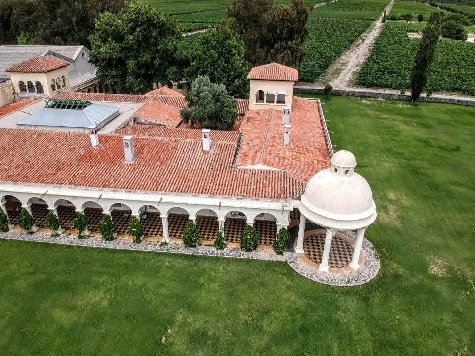 An aerial view of a large house with a gazebo in the middle of a lush green field.