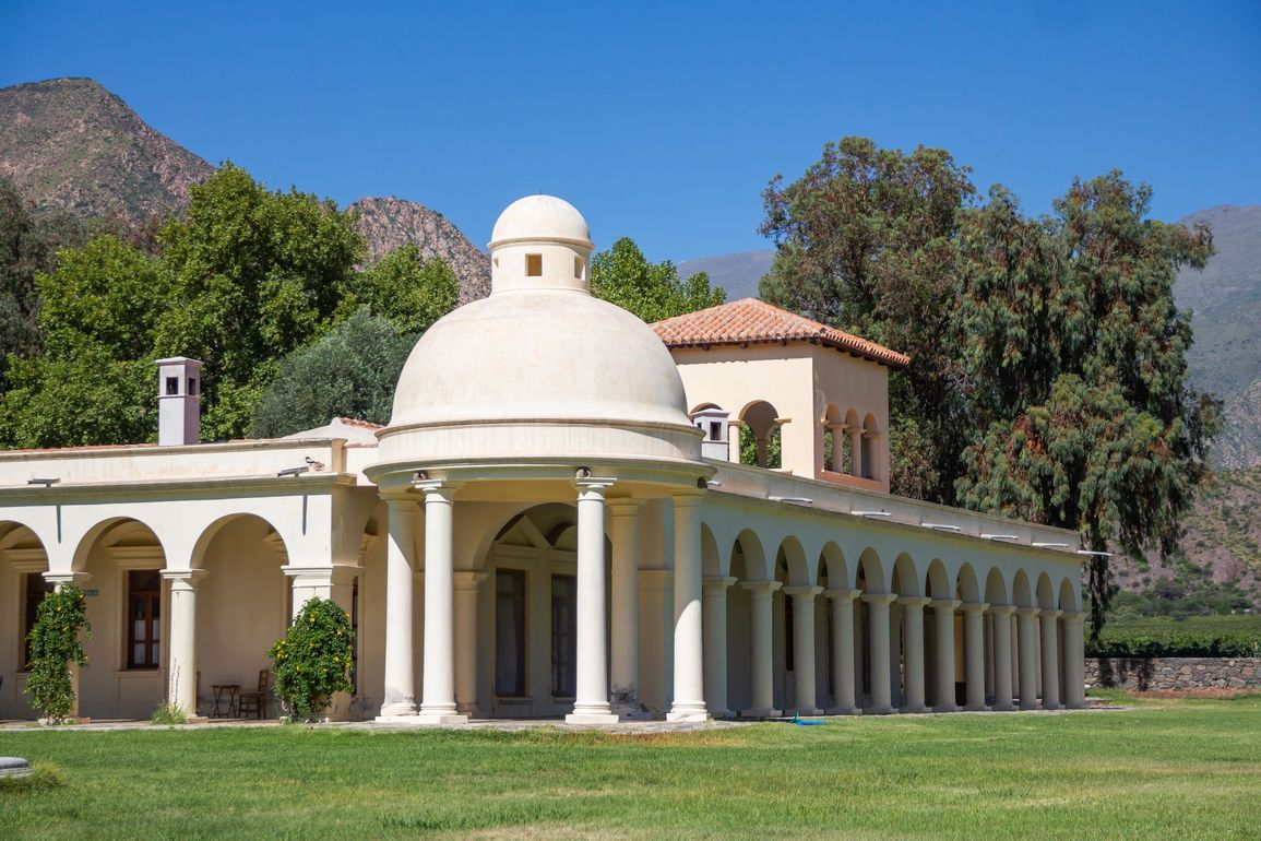 A large white building with a dome on top of it is sitting on top of a lush green field.