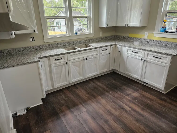 White kitchen cabinets with granite countertops and dark wood flooring.