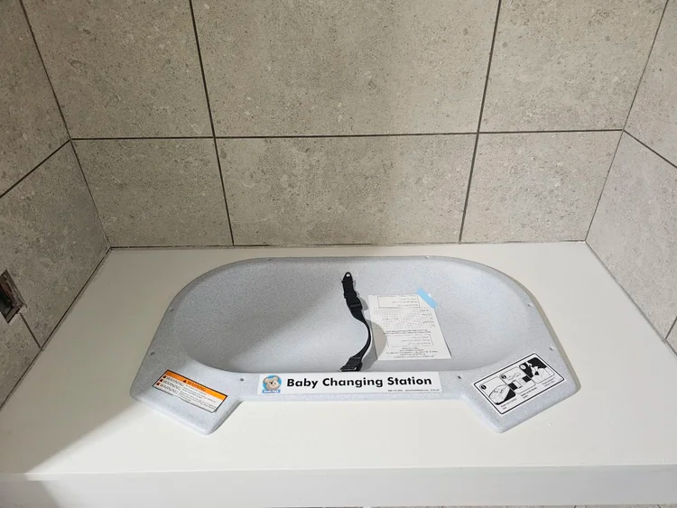 Baby changing station mounted on a white surface, against tiled walls.