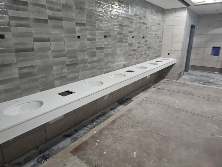 Bathroom under construction with a long counter with multiple sinks, gray tiled walls.