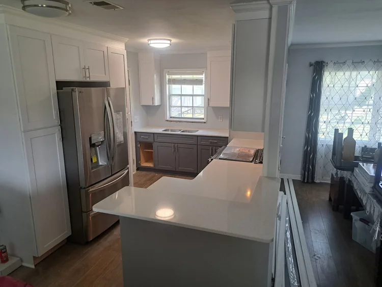Kitchen remodel with white and gray cabinets, stainless steel refrigerator, and light countertops.