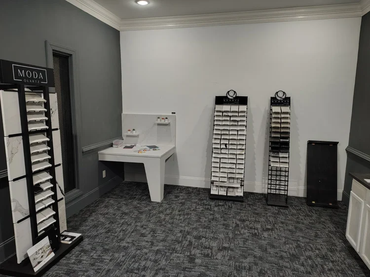 Tile showroom interior with display racks, samples on a white desk, and dark gray carpet.