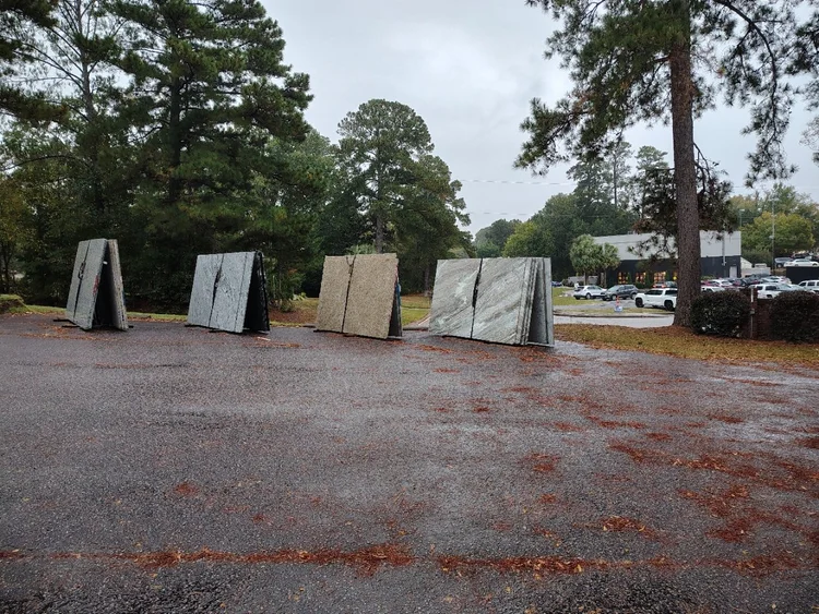 Four large, rectangular marble slabs standing upright on an asphalt surface, trees in the background.