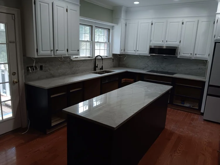 Kitchen remodel featuring white cabinets, dark island, marble countertops, and dark wood flooring.