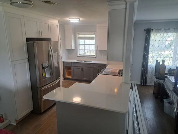 Newly renovated kitchen with white cabinets, gray countertops, and stainless steel refrigerator.