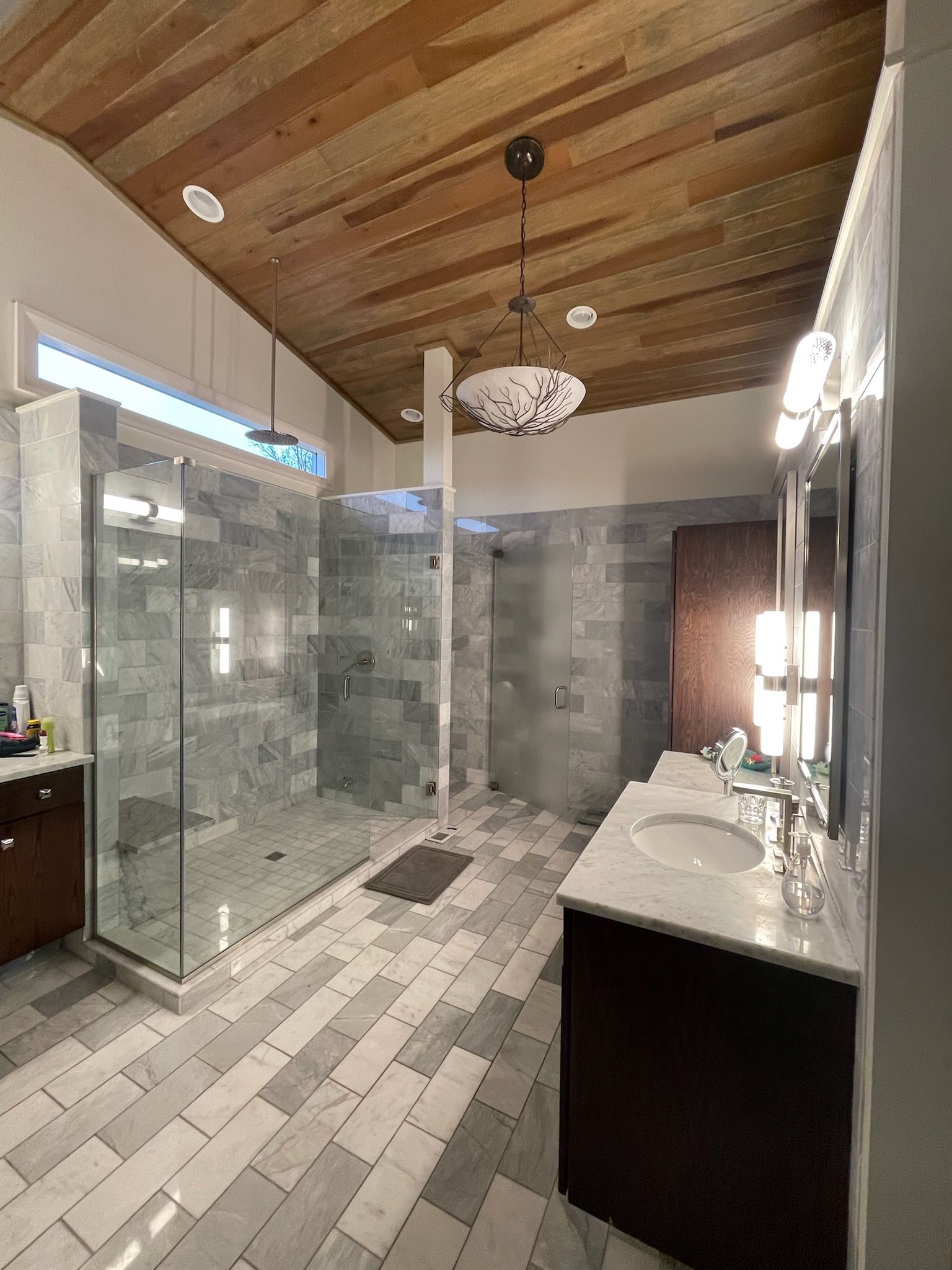 A bathroom with a walk in shower , sink , mirror and wooden ceiling.