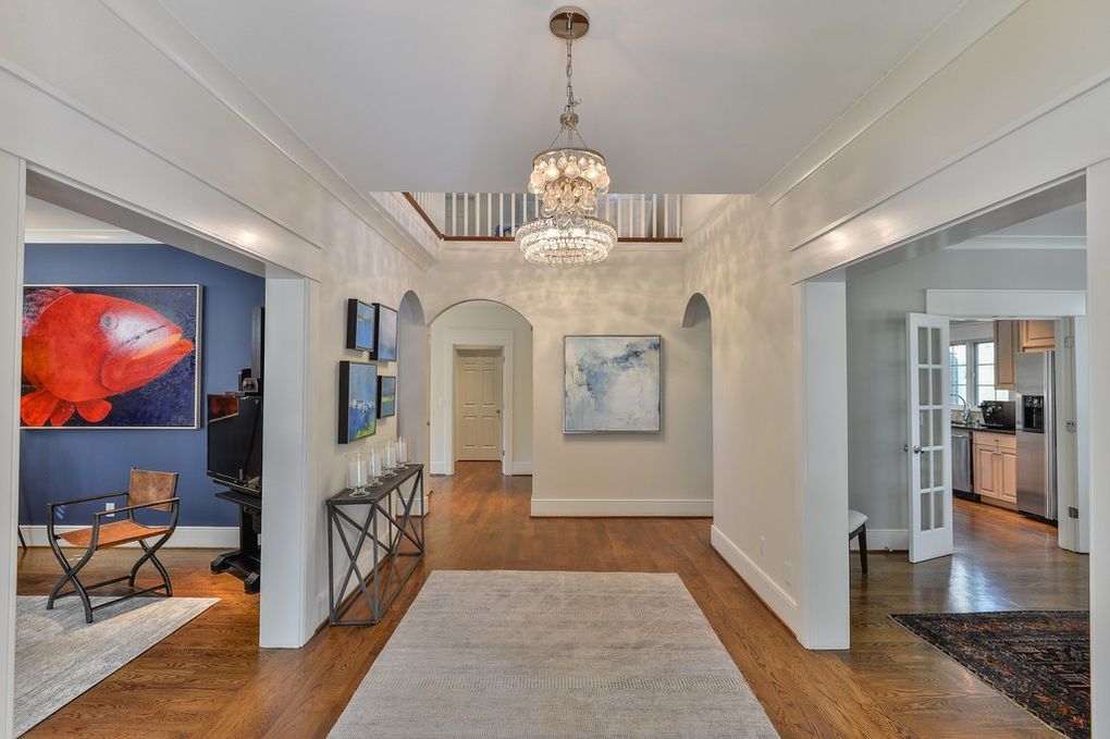 A hallway in a house with hardwood floors and a chandelier hanging from the ceiling.