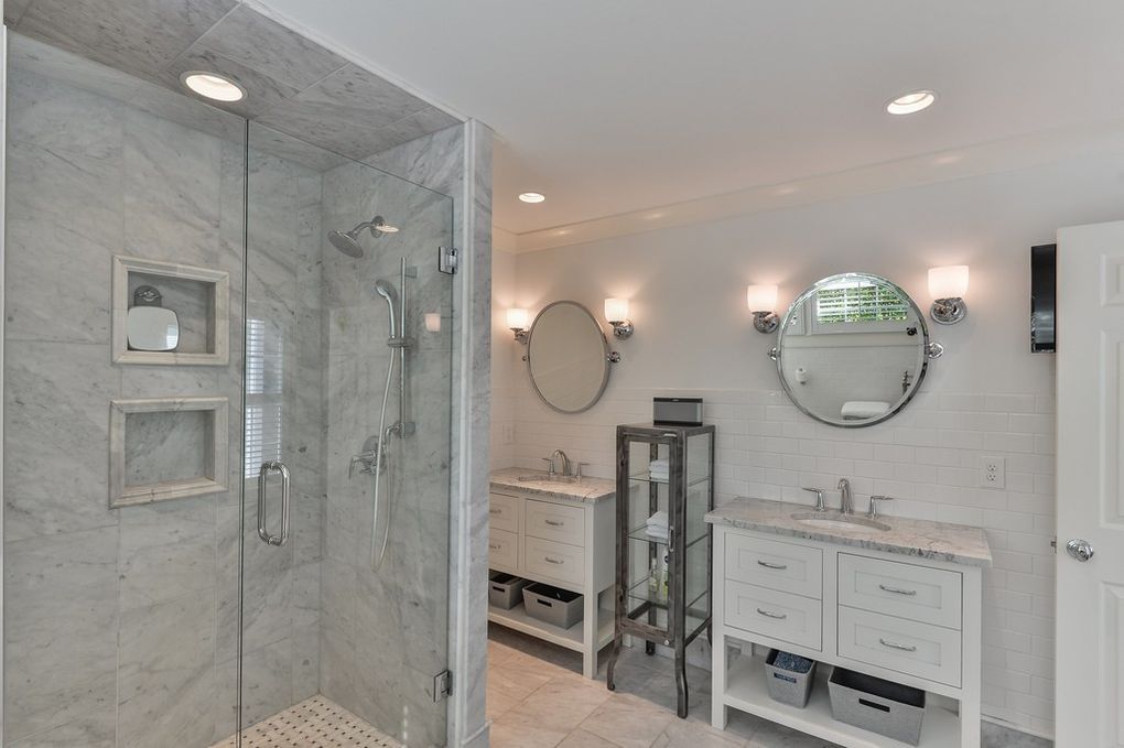 A bathroom with a walk in shower , sink , mirror and vanity.