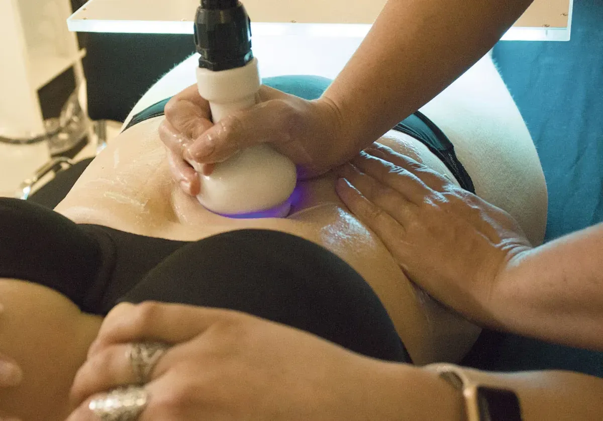 Une personne reçoit un traitement de remodelage corporel non invasif au niveau de l'abdomen ; un technicien utilise un appareil à lumière bleue.