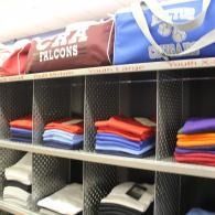 Folded sports jerseys stacked on cubby shelves, including red, blue, white, and purple uniforms.