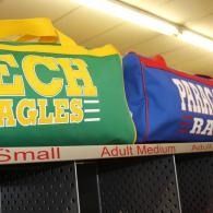 Green and blue sports jerseys hanging on a rack, labeled sizes Small and Adult Medium.