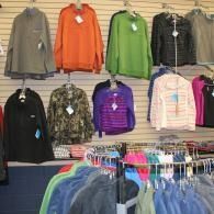 Clothing store display with colorful jackets and hoodies hanging on wall racks above folded apparel.