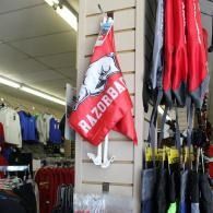 Red and black Razorbak flag hanging in a sports store beside other shirts and gear.