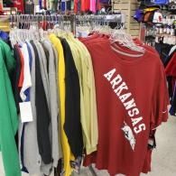 Rack of hanging shirts, including a red Arkansas T-shirt in the foreground, in a store.