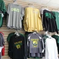 Sports team T-shirts hanging on a store wall, mostly green, gray, yellow, and black.