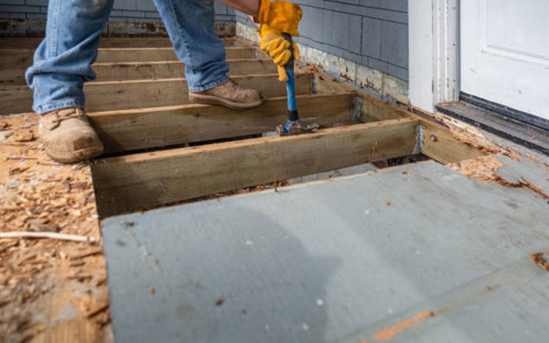 A man is working on a wooden deck with a hammer.