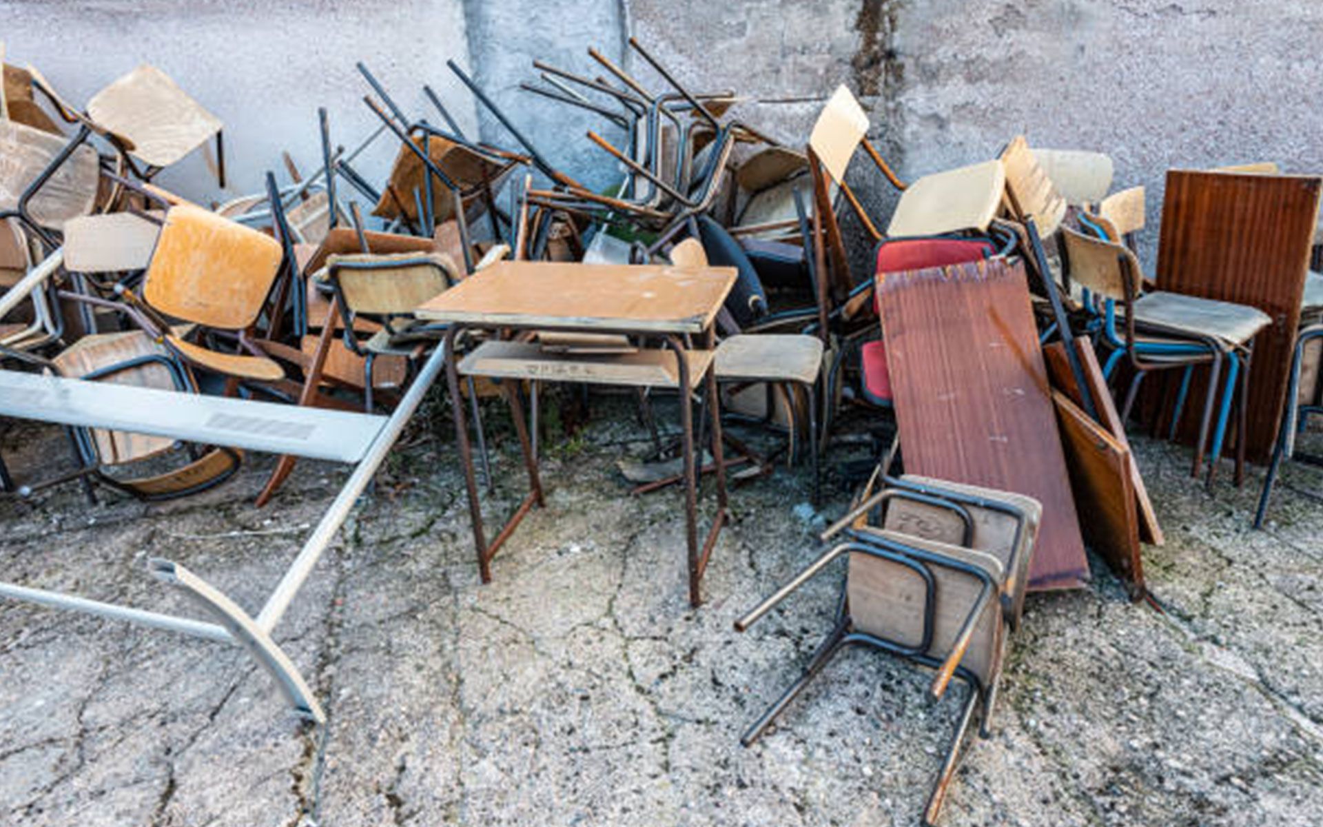 A pile of tables and chairs are stacked on top of each other on the ground.