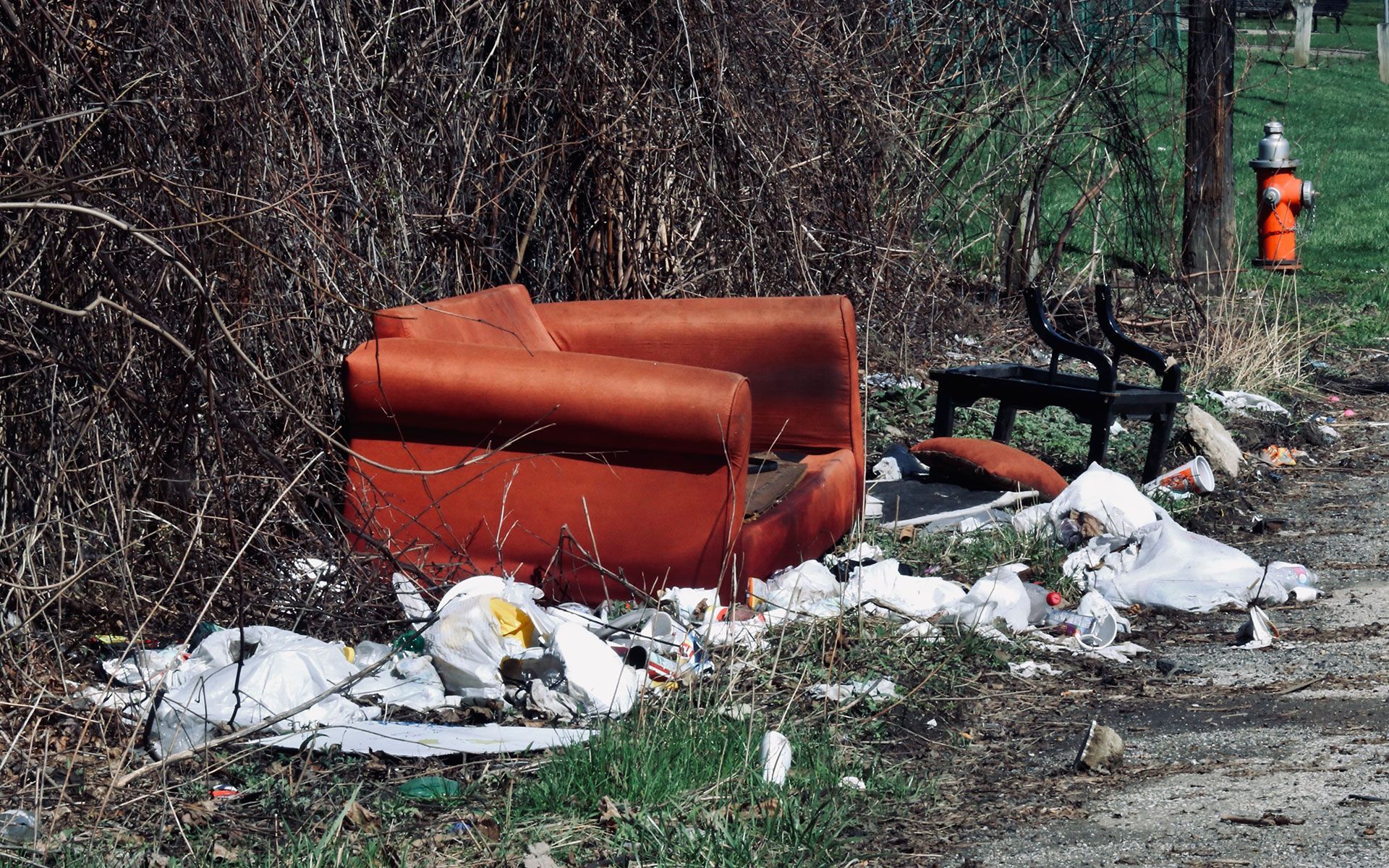 A red couch is sitting on the side of a dirt road next to a fire hydrant.